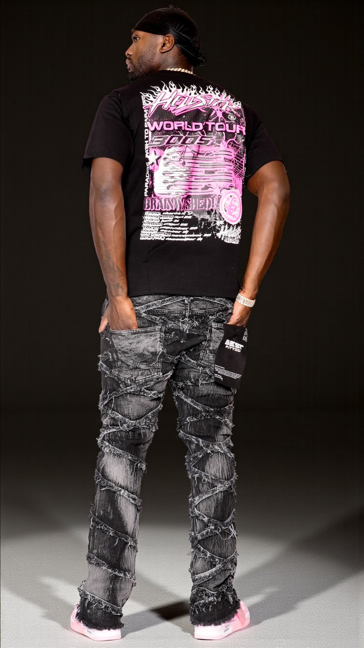 Person wearing a black t-shirt with graphic designs and distressed jeans on a dark background