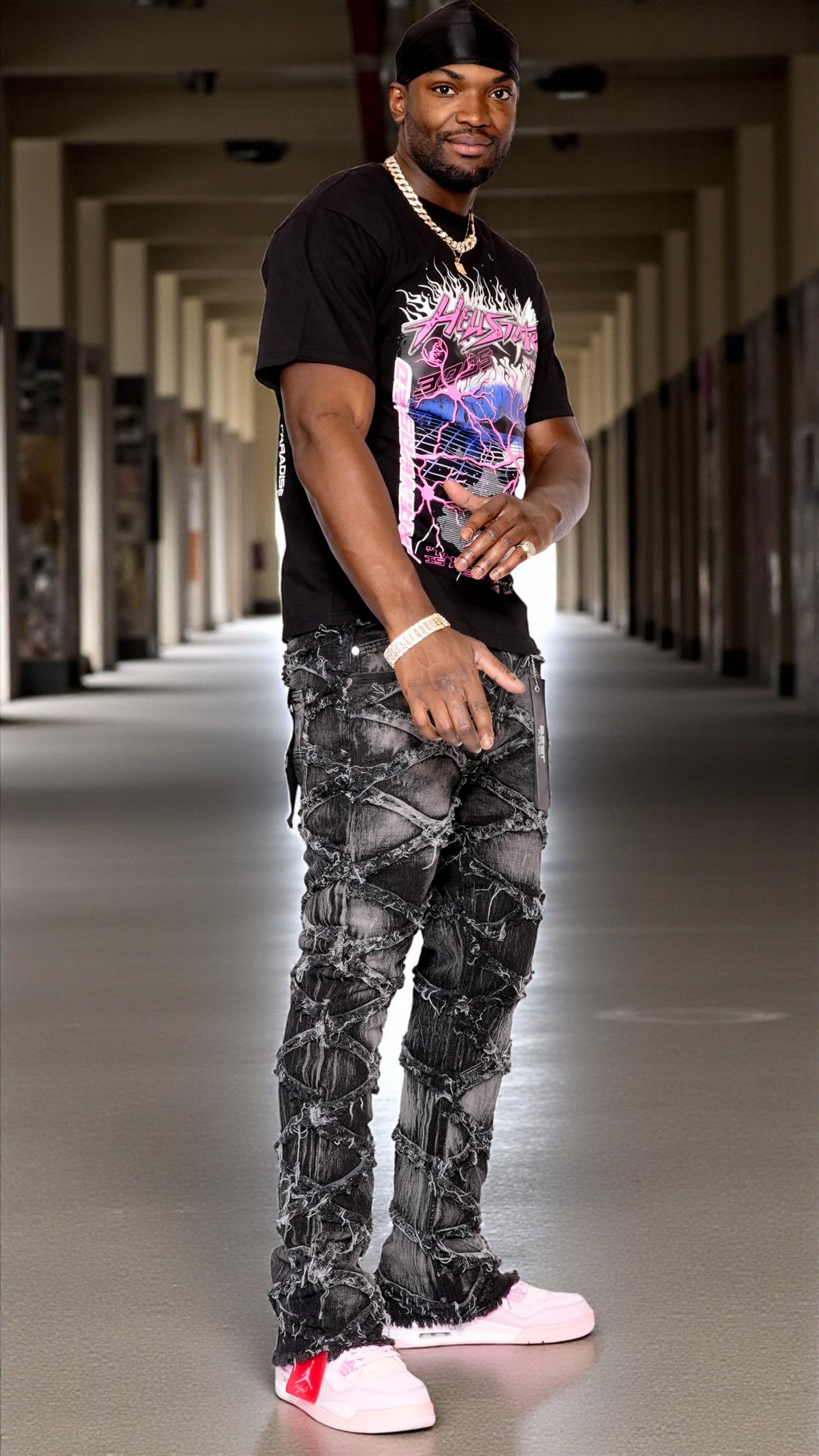 Man wearing a black t-shirt with a colorful graphic and patterned pants in a hallway.