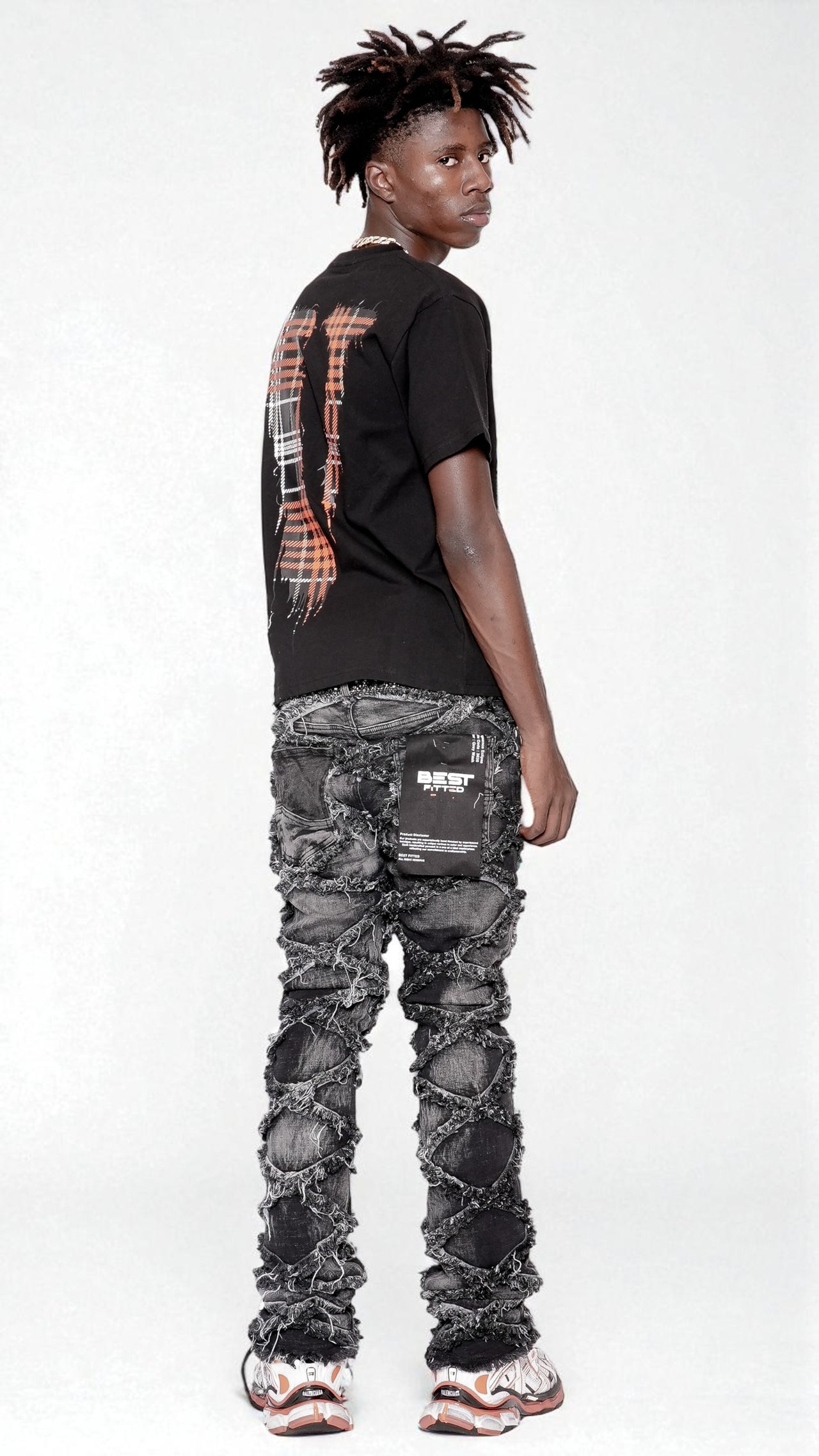 Person wearing a black t-shirt with a plaid design on the back and camouflage pants against a white background