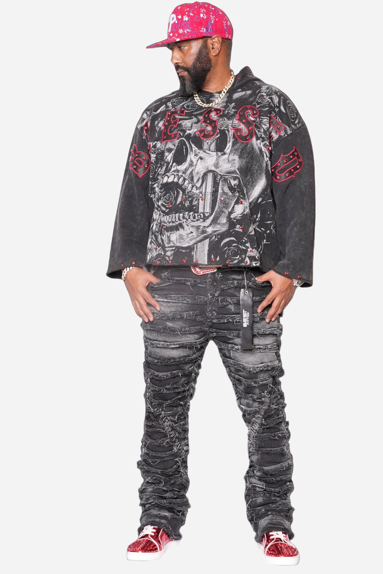 Person wearing a black graphic sweatshirt with red accents, gray jeans, and red sneakers on a black background.