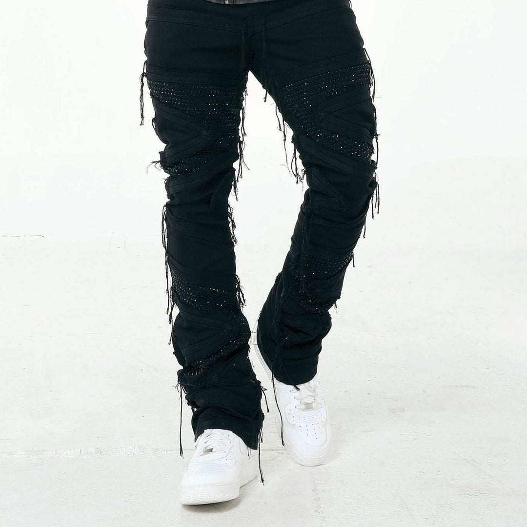 Black distressed jeans with rhinestone embellishments worn by a person on a white background