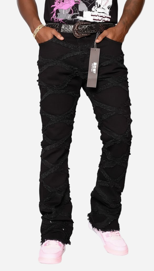 Person wearing black distressed jeans with a tag, standing against a white background