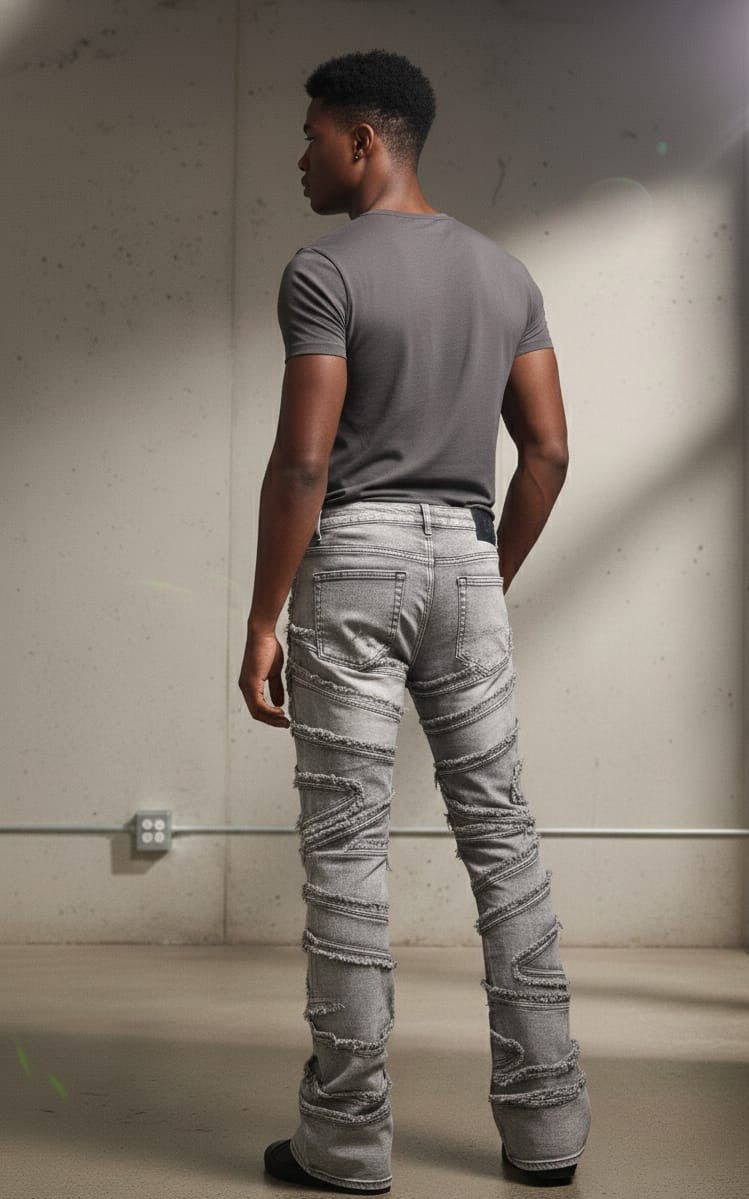 Man wearing a gray t-shirt and ripped jeans standing against a plain wall.