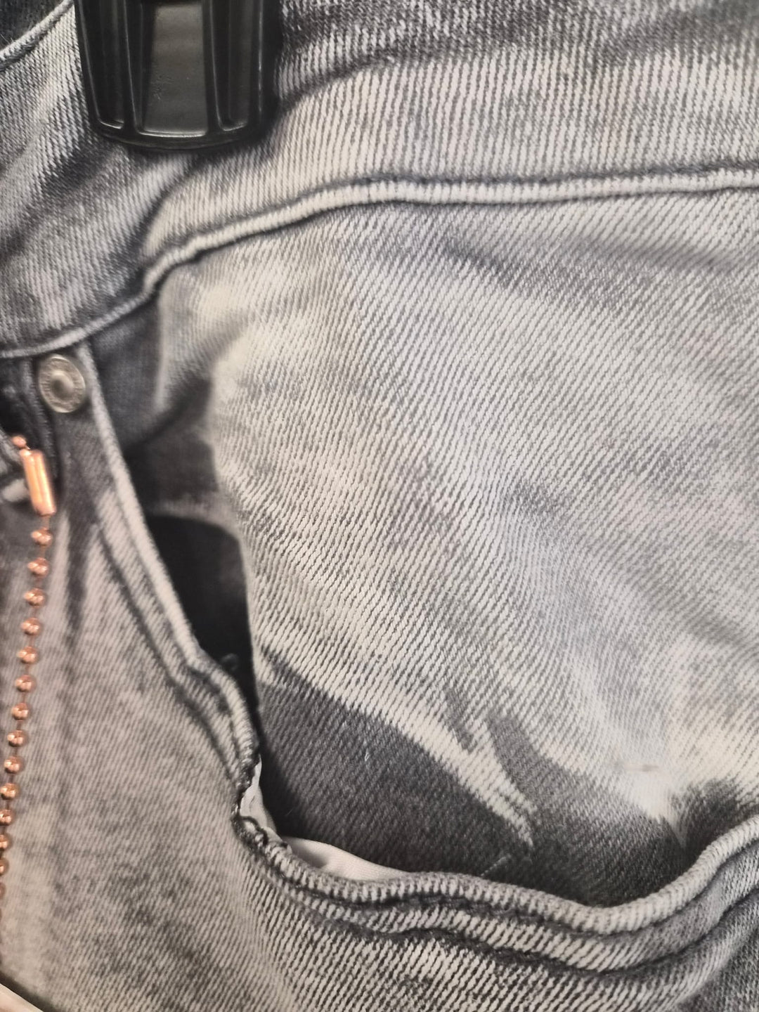 Close-up of a gray denim pocket with a zipper and button detail.
