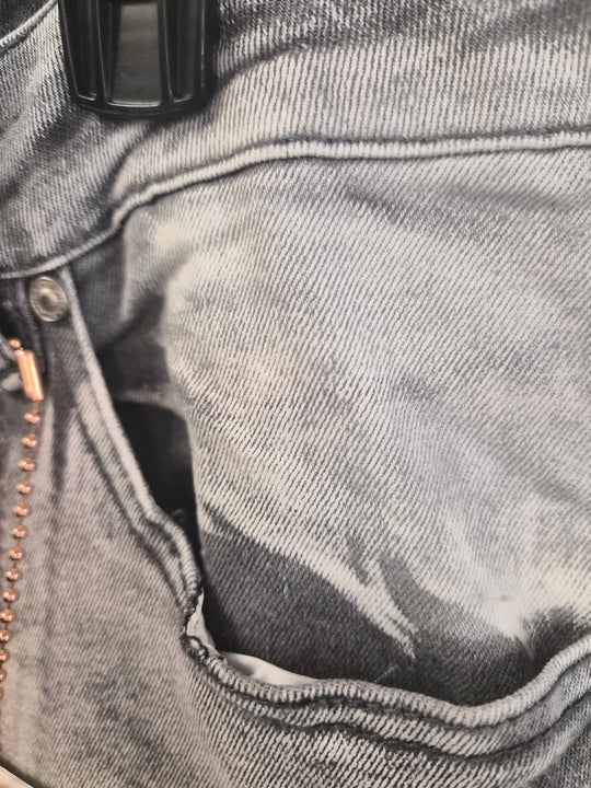 Close-up of a gray denim pocket with a zipper and button detail.