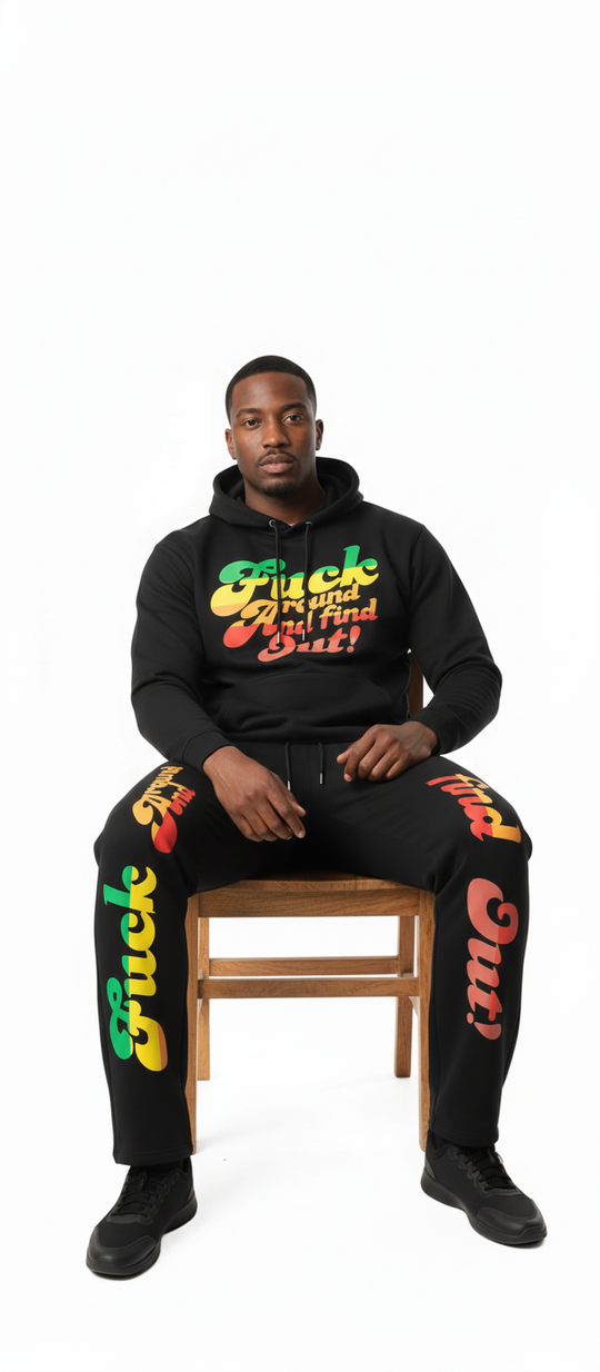 Person wearing a black hoodie and pants with colorful text sitting on a wooden chair against a white background
