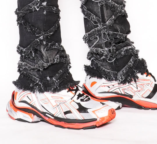 White sneakers with orange accents worn with ripped black jeans on a white background